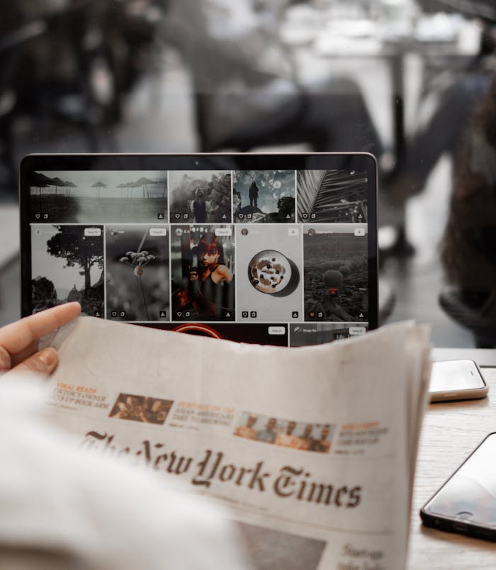 ours-journey A person reading a newspaper while browsing images on a laptop, symbolizing remote work lifestyle.
