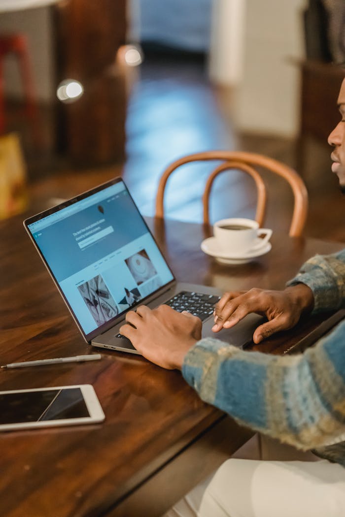 services-01 Crop unrecognizable Black male freelancer in casual clothes sitting at wooden table with laptop and typing on keyboard of modern interior