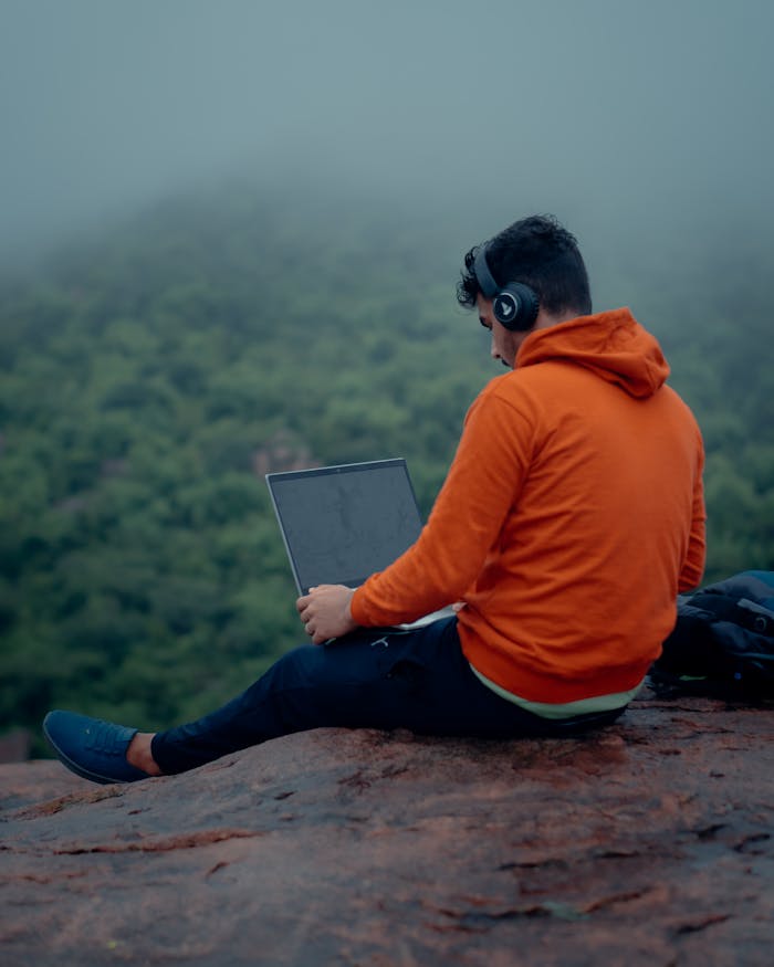 about-02 Individual wearing headphones works on a laptop atop a scenic mountain in Bengaluru, India.
